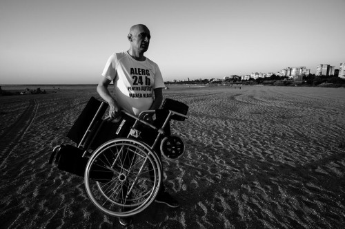 bărbat pe plajă, ține în mâini un scaun rulant