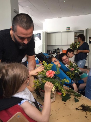 tatăl ajută fiica în scaun rulant să poata atinge florile dintr-un vas