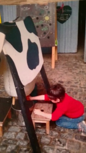 copil mulgănd o vacă de jucărie, la o fermă