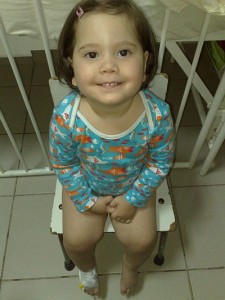 Fetiță de aproximativ doi ani zambind, stând pe scăunel într-un spital