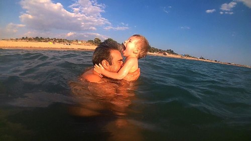 băiat râzând, ținut de tată în brațe, în apă