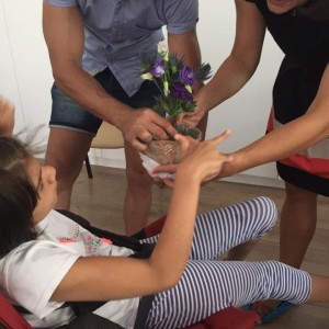 tatăl ajută fiica în scaun rulant să poata atinge florile dintr-un vas