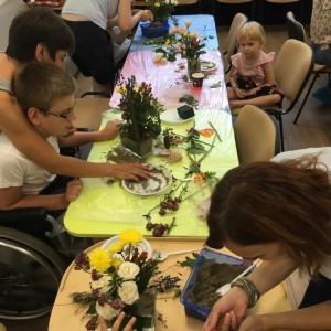 copii cu dizabilități la masă, lucrează aranjamente florale ajutați de adulți