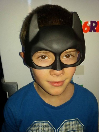 băiat, poarta o mască de supererou, privește zâmbind spre cameră