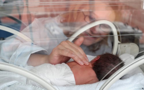 bebeluș prematur în incubator, mama privește către el
