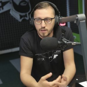 bărbat cu ochelari, în fața microfonului într-un studio de radio, pe cap are căști