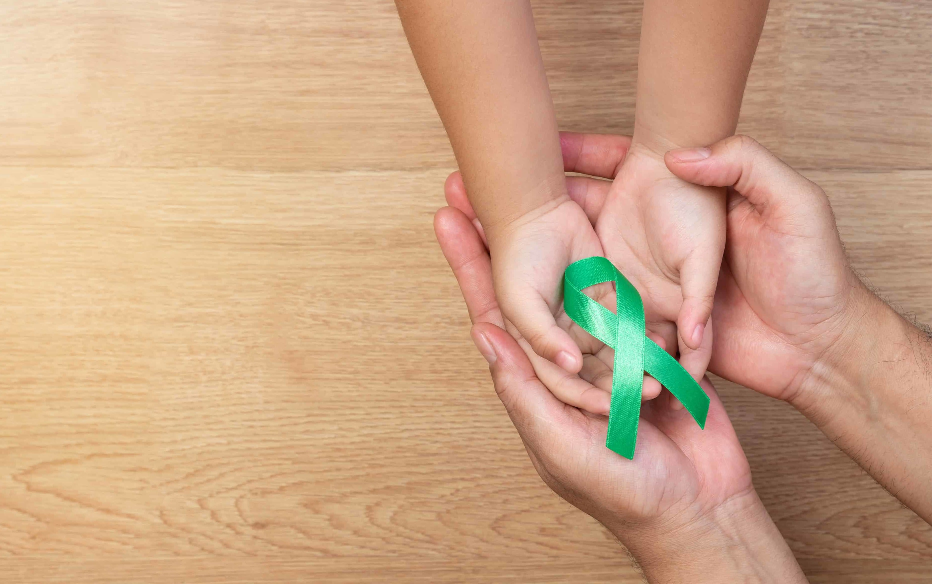 palmele unui adult țin palmele unui copil, ambii țin o panglică verde, simbolul conștientizării bolilor mitocondriale