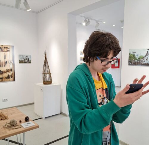 Un tânăr de 14 ani folosește Google lens pe telefonul mobil pentru a identifica ce se află într-una dintre fotografiile din expoziție.