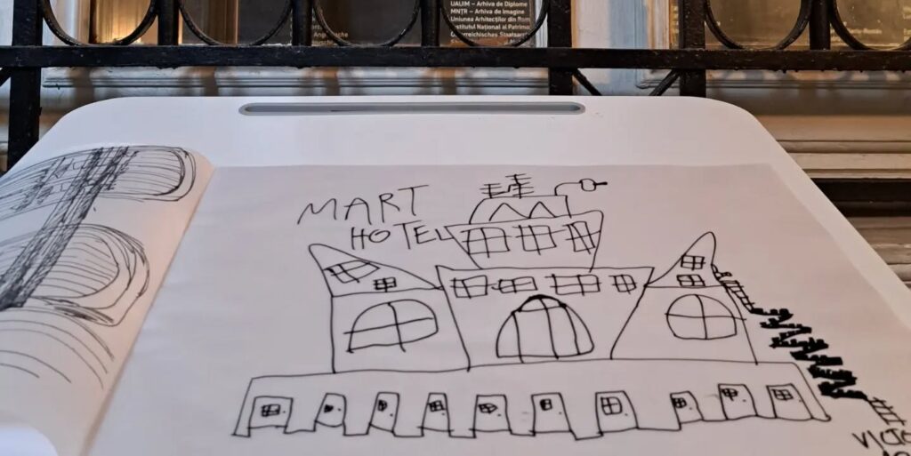 În prim plan, desenul unui hotel fantezie, imaginare, făcut de un băiat de 12 ani, autist. În plan secund, panoul de sală al expoziției. Textul spune: "fantezie. Stația 1 București. "