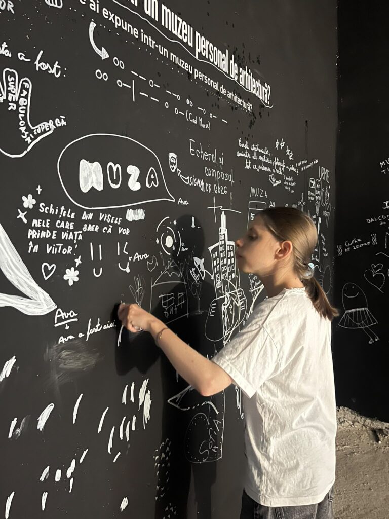 Olga, tânără de 18 ani, scrie cu marker pe un perete, alături de alte răspunsuri la întrebarea scrișa deasupra:"tu ce ai expuneîntr-un muzeu personal de arhitectură?".